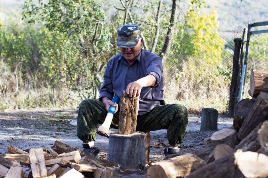Old man chops wood sitting